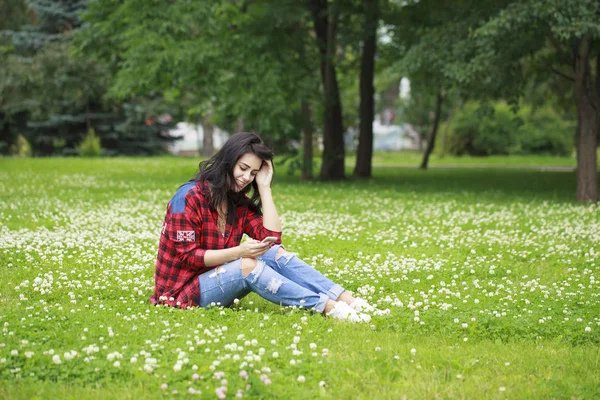 Junge Frau liegt im Gras und liest eine Nachricht auf einem Handy — Stockfoto