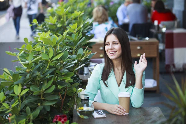 Mujer sentada en un café da la bienvenida agitando su mano — Foto de Stock