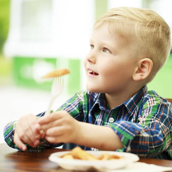 Blond chlapec jíst smažené brambory v kavárně — Stock fotografie