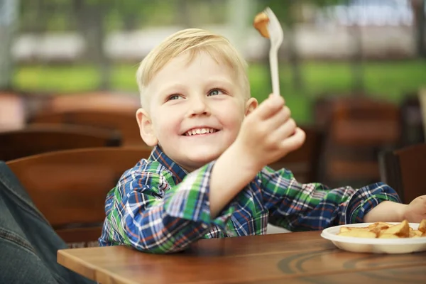 Blond chlapec jíst smažené brambory v kavárně — Stock fotografie