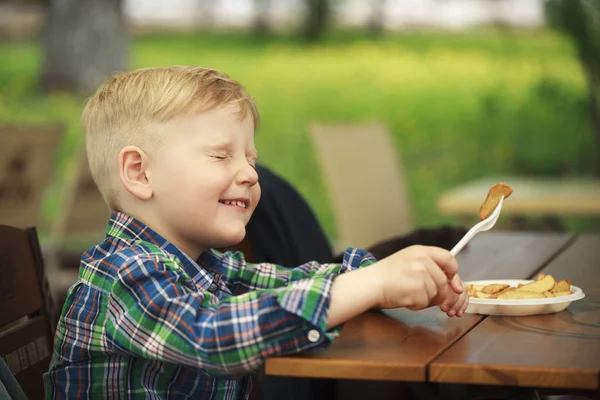 Blonde little boy eating fried potatoes at a cafe — Stock Photo, Image