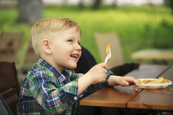 Blonde little boy eating fried potatoes at a cafe — Stock Photo, Image