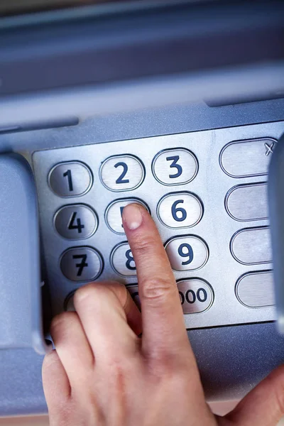 Close up of hand entering pin at an ATM. Finger about to press a pin code on a pad. Security code on an Automated Teller Machine. Female arms, ATM - entering pin