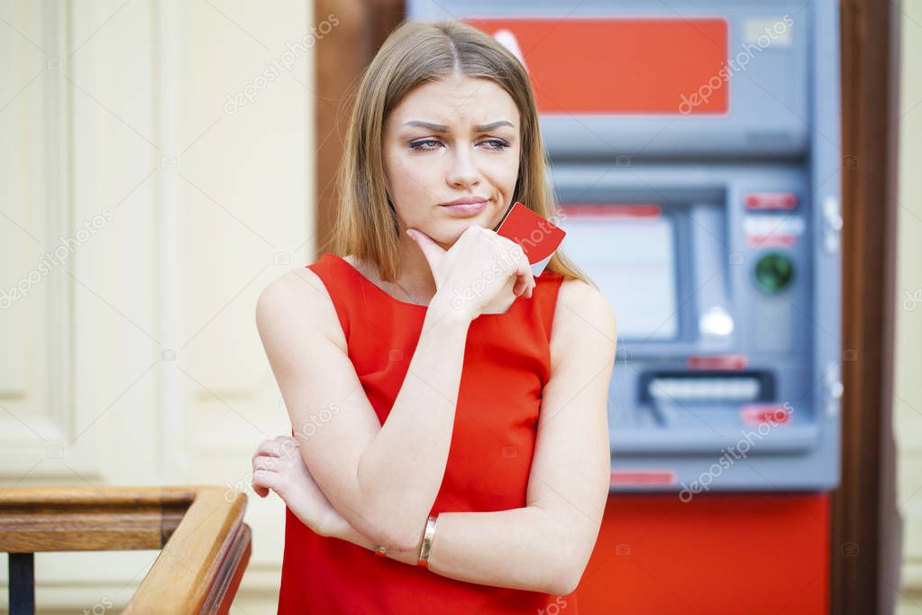 Frustrated young woman stands on against ATM