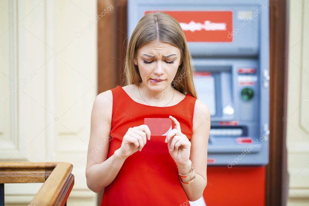 Frustrated young woman stands on against ATM