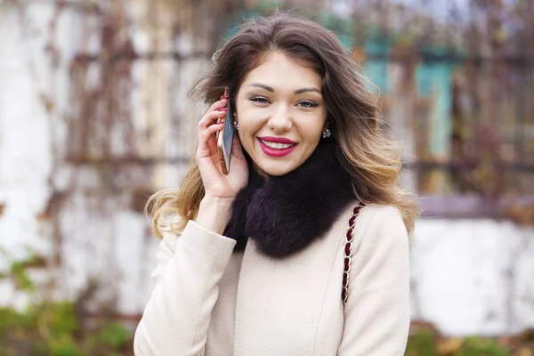 Portrait of happy young brunette woman in beige coat talking on — Stock Photo, Image