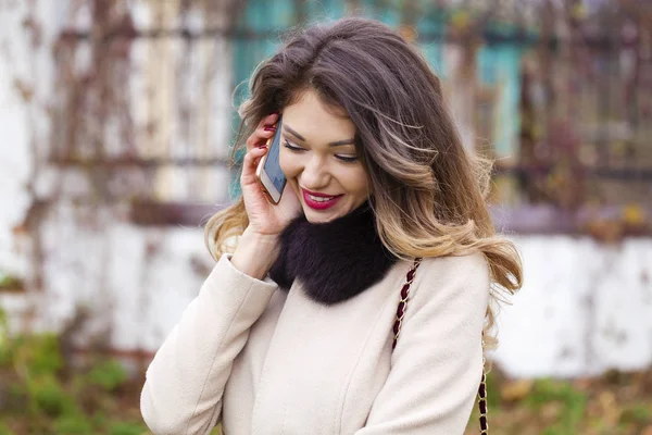 Portrait de heureuse jeune femme brune en manteau beige parlant sur — Photo