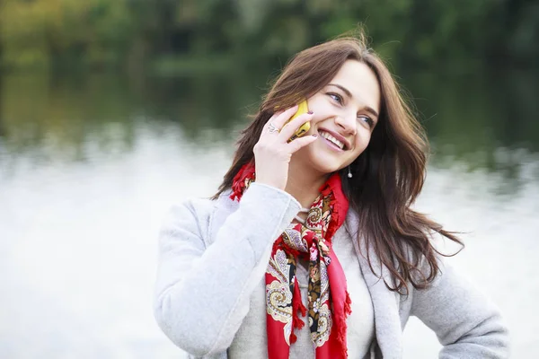 Porträtt av glad ung brunett kvinna i beige kappa talar på — Stockfoto