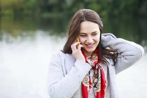 Portrait of happy young brunette woman in beige coat talking on — Stock Photo, Image