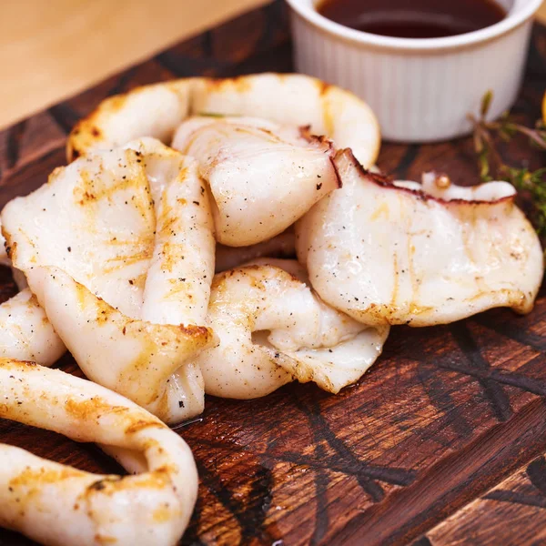 Anelli di calamari grigliati su una tavola di legno con salsa — Foto Stock