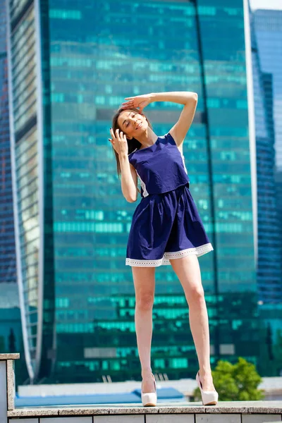 Young woman in a blue dress is stretching near skyscrapers — Stock Photo, Image