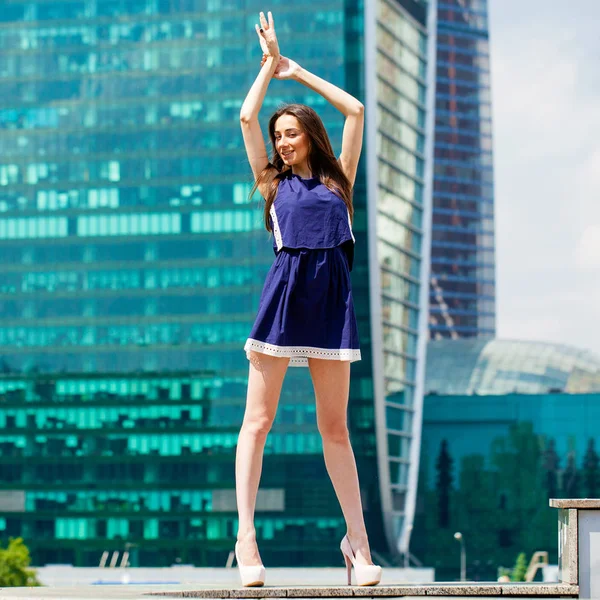 Fiatal nő, egy kék ruhát, nyújtás, felhőkarcoló közelében — Stock Fotó