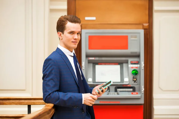 Ein junger Geschäftsmann steht in der Nähe eines Geldautomaten in einem Einkaufszentrum — Stockfoto