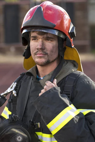 Porträt eines jungen Feuerwehrmannes vor dem Hintergrund eines Feuerwehrfahrzeugs — Stockfoto