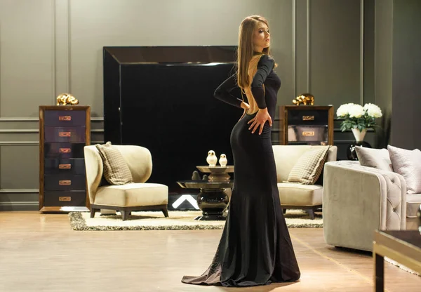 Mulher loira sexy em um vestido de noite preto posando em um mobiliário — Fotografia de Stock