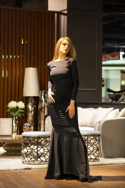 Sexig blond kvinna i svart aftonklänning poserar i en möbel — Stockfoto