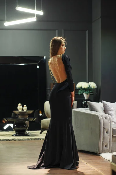 검은 저녁 드레스를 입고 가구에 포즈를 취하는 섹시 한 금발 여성 — 스톡 사진