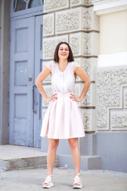 Pembe etekli, beyaz bluzlu, esmer bir kadın.