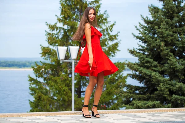 Young beautiful model in red dress walking on the summer street — Stock Photo, Image