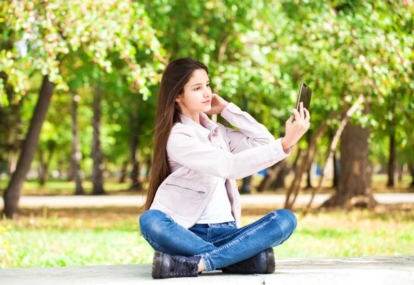Brunette meisje fotografeert zichzelf op een mobiele telefoon tijdens het zitten — Stockfoto