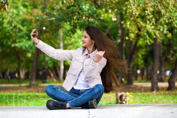 Brunette girl photographs herself on a cell phone while sitting — Stock Photo, Image