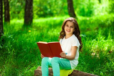 Orman ağaç kütüğü üzerinde oturup kitap ile sevimli küçük kız