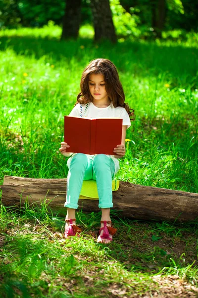 Affascinante bambina nella foresta con libro seduto sul tronco d'albero — Foto Stock