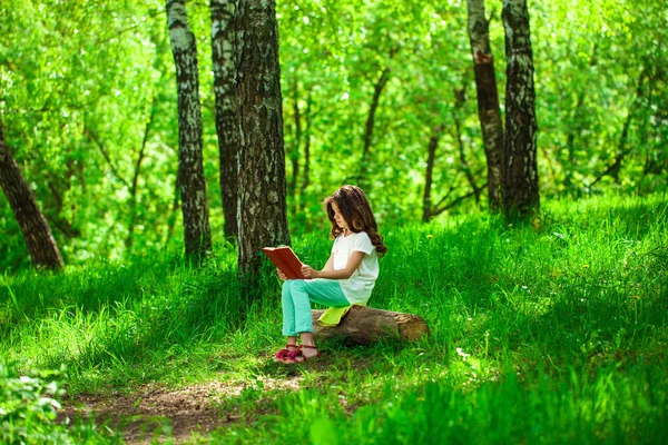 Urocze dziewczynki w lesie z książki siedzi na pniu drzewa — Zdjęcie stockowe