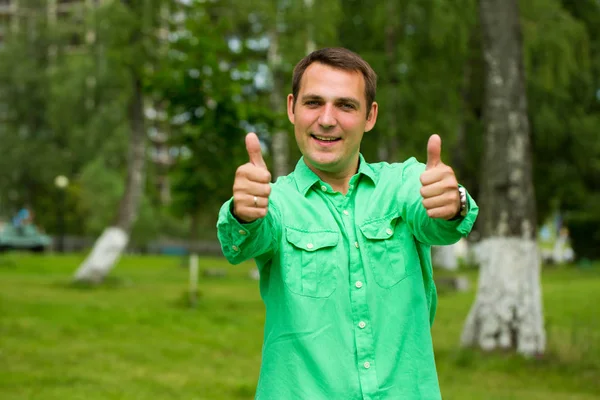 Jovem homem bonito com o polegar para cima em uma camisa verde no backgro — Fotografia de Stock