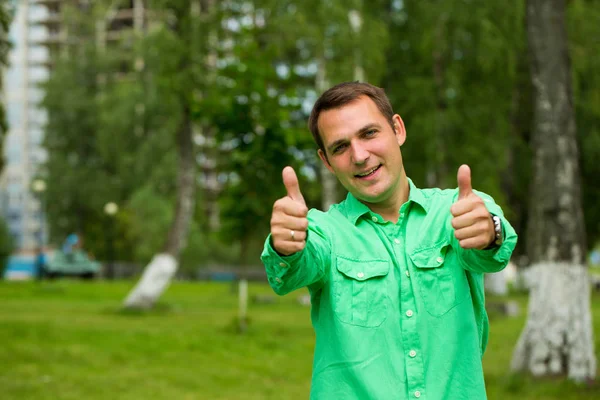 年轻英俊的男人，用大拇指在一件绿色的衬衫上的背景 — 图库照片