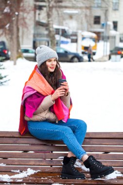 Kış parkında elinde bir bardak kahveyle genç bir kız.