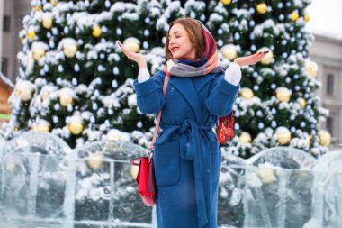 Mavi ceketli mutlu genç kız kış sokağında poz veriyor.