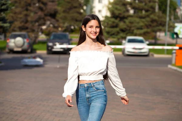 Joven hermosa morena mujer en jeans y blusa blanca caminando —  Fotos de Stock