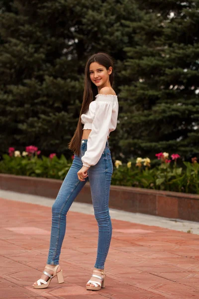Bella ragazza bruna elegante in jeans blu e camicetta bianca — Foto Stock