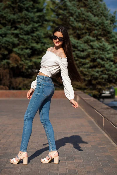 Ziemlich stylisches brünettes Mädchen in blauen Jeans und weißer Bluse — Stockfoto