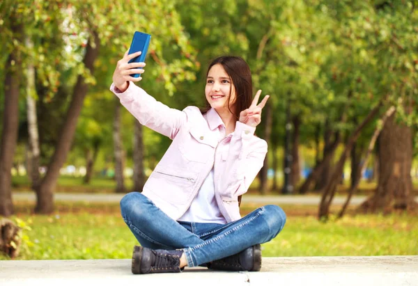 Malá brunetka se při sezení sama fotografovala na mobilním telefonu — Stock fotografie
