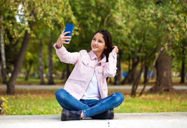 Brunette girl photographs herself on a cell phone while sitting — Stock Photo, Image