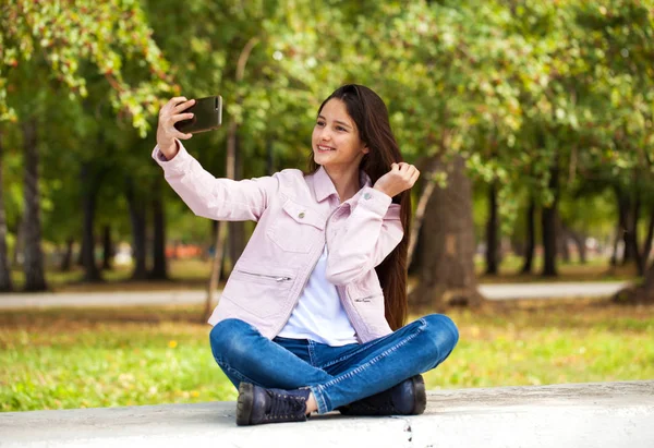 Brunetka dziewczyna fotografie sama na a komórka telefon podczas siedzący — Zdjęcie stockowe