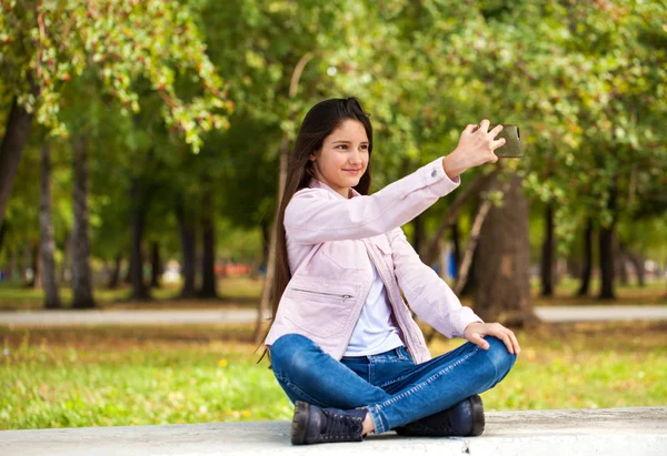 Morena chica fotografías a sí misma en un teléfono celular mientras está sentado —  Fotos de Stock