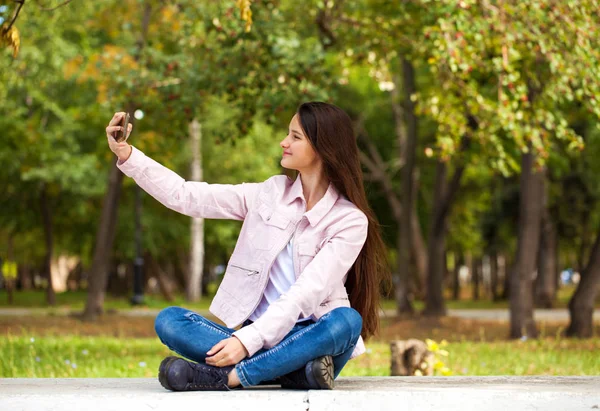 Bruna ragazza fotografa se stessa su un cellulare mentre è seduta — Foto Stock