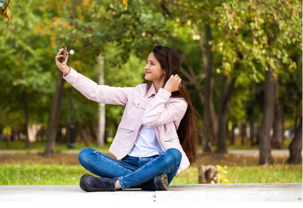 Brunette girl photographs herself on a cell phone while sitting — Stock Photo, Image