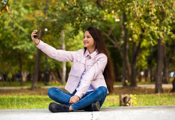 Brunette girl photographs herself on a cell phone while sitting — Stock Photo, Image