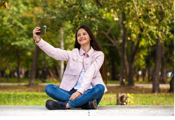 Μελαχρινή κορίτσι φωτογραφίες τον εαυτό της σε ένα κινητό τηλέφωνο ενώ κάθεται — Φωτογραφία Αρχείου