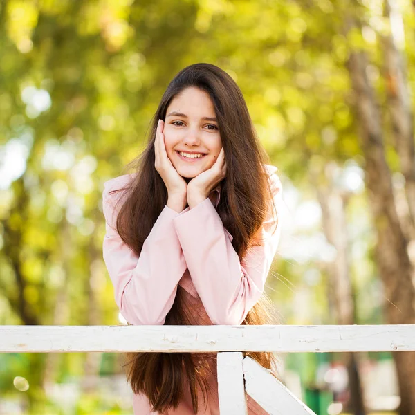 Porträt eines jungen brünetten Mädchens in rosa Mantel auf einem Hintergrund o — Stockfoto