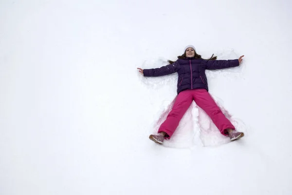 Schneeengel. junges schönes Mädchen im Skianzug liegt im Schnee — Stockfoto