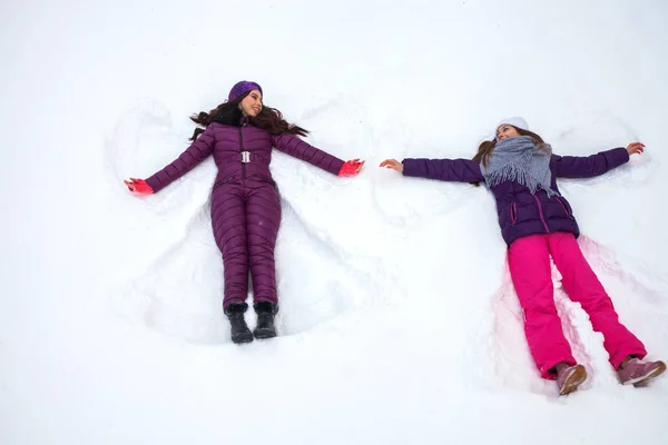 Sneeuwengelen. Twee jonge mooie meisjes in een skipak ligt op de — Stockfoto