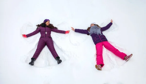 Sneeuwengelen. Twee jonge mooie meisjes in een skipak ligt op de — Stockfoto