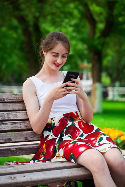 Telefonisch. schönes Mädchen im Sommerkleid sitzt auf einem pa — Stockfoto