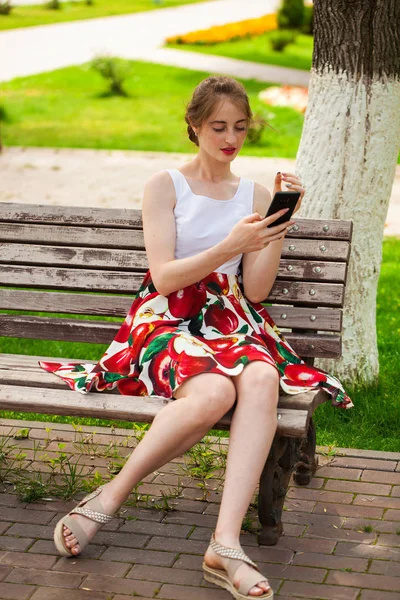 Telefonisch. schönes Mädchen im Sommerkleid sitzt auf einem pa — Stockfoto