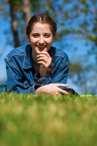 Krásná mladá brunetka ležící na zelené trávě — Stock fotografie